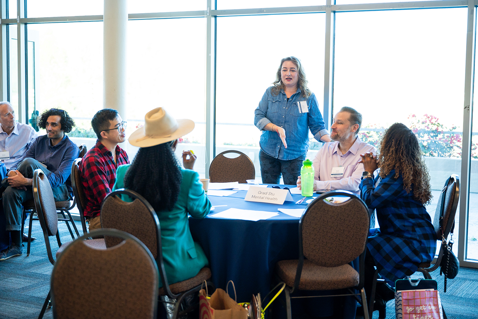 people seated around circular tables conversing one person standing