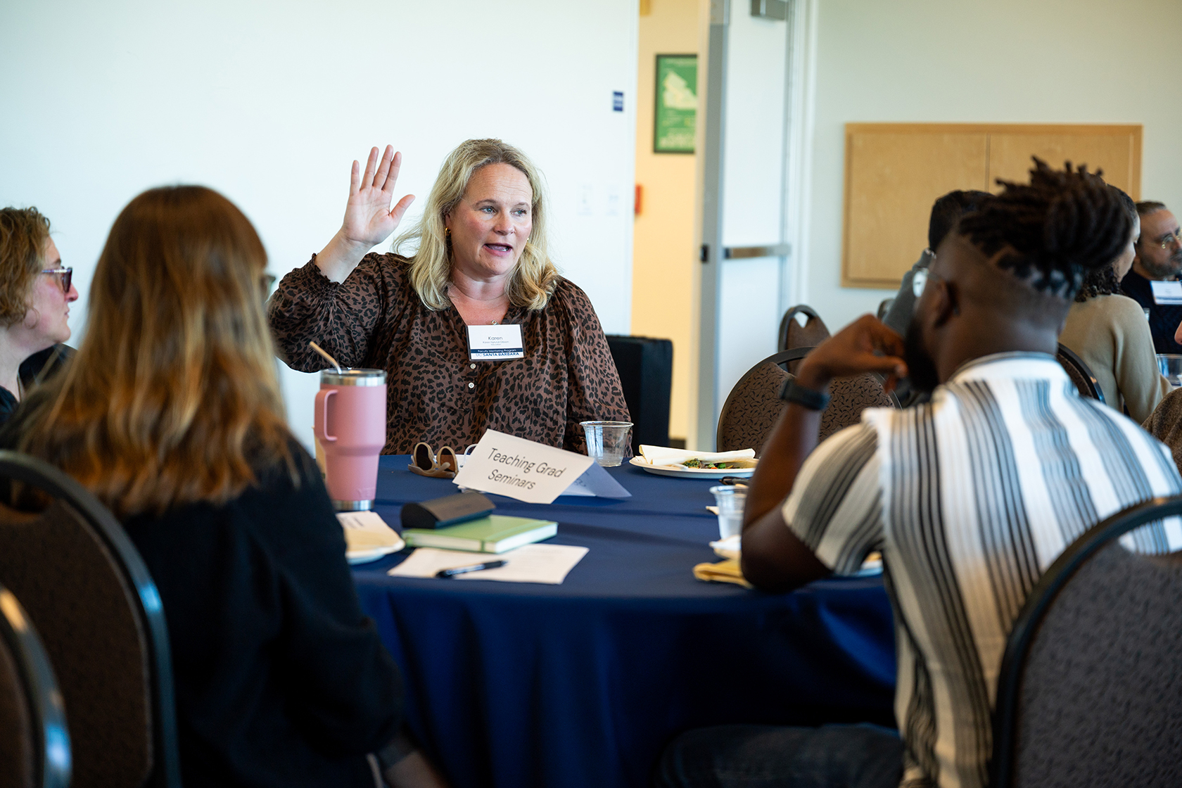 photo of four people seated at a table one person raising their hand