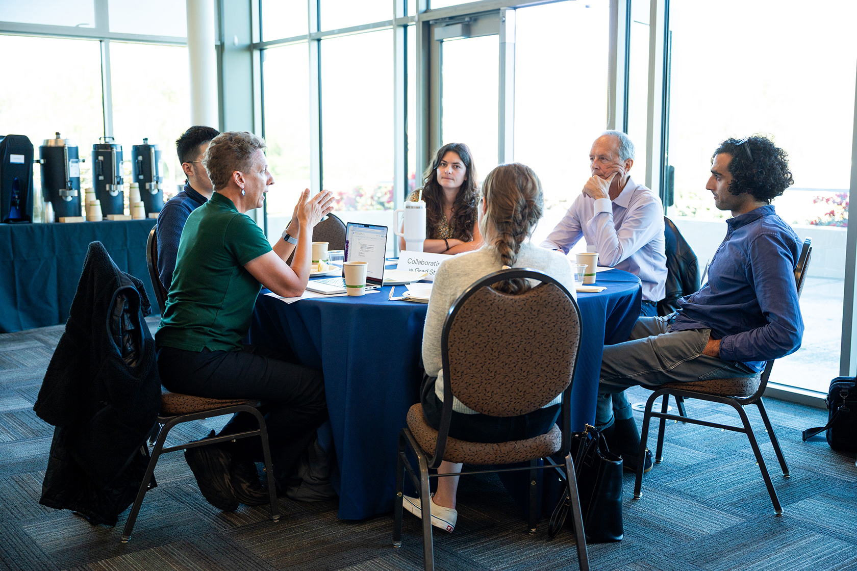 photo of six people seated at a circular table talking