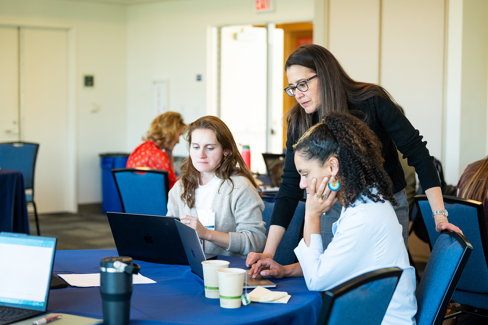 two seated people with one standing leaning over to glance down