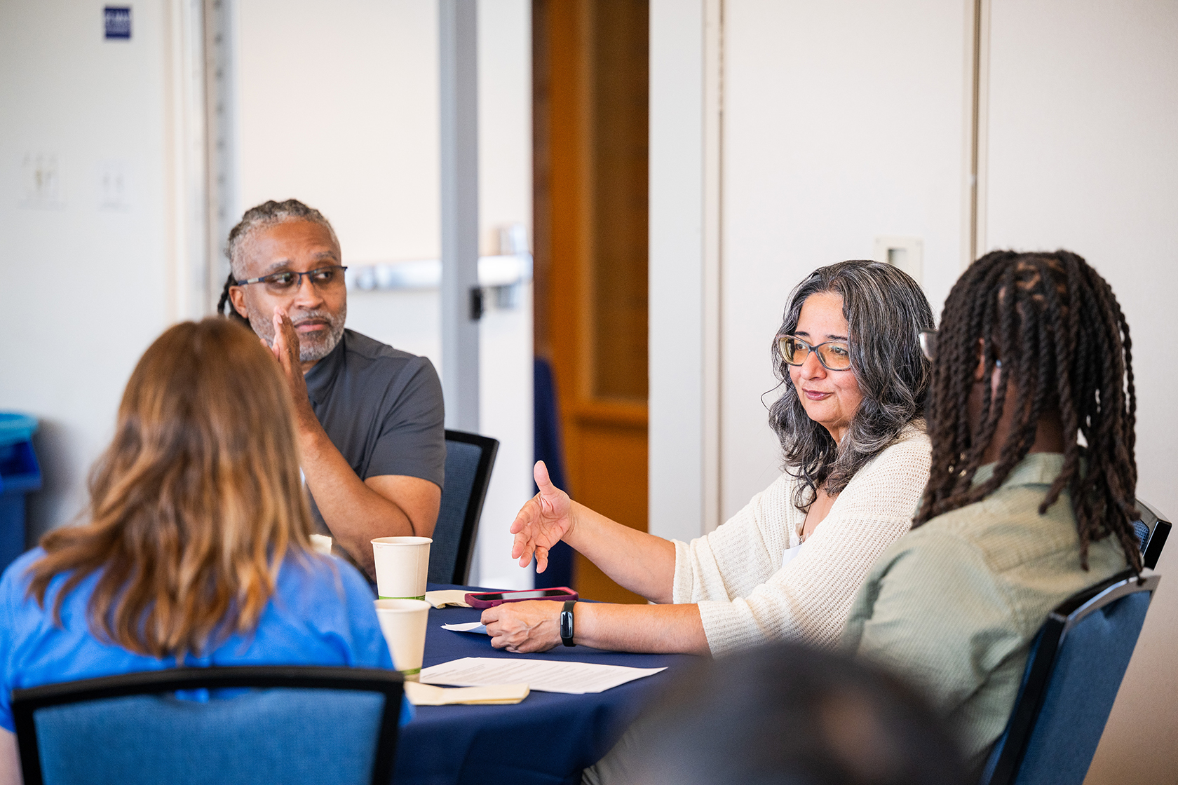 Woman in glasses appears to be speaking as participants engage along in conversation