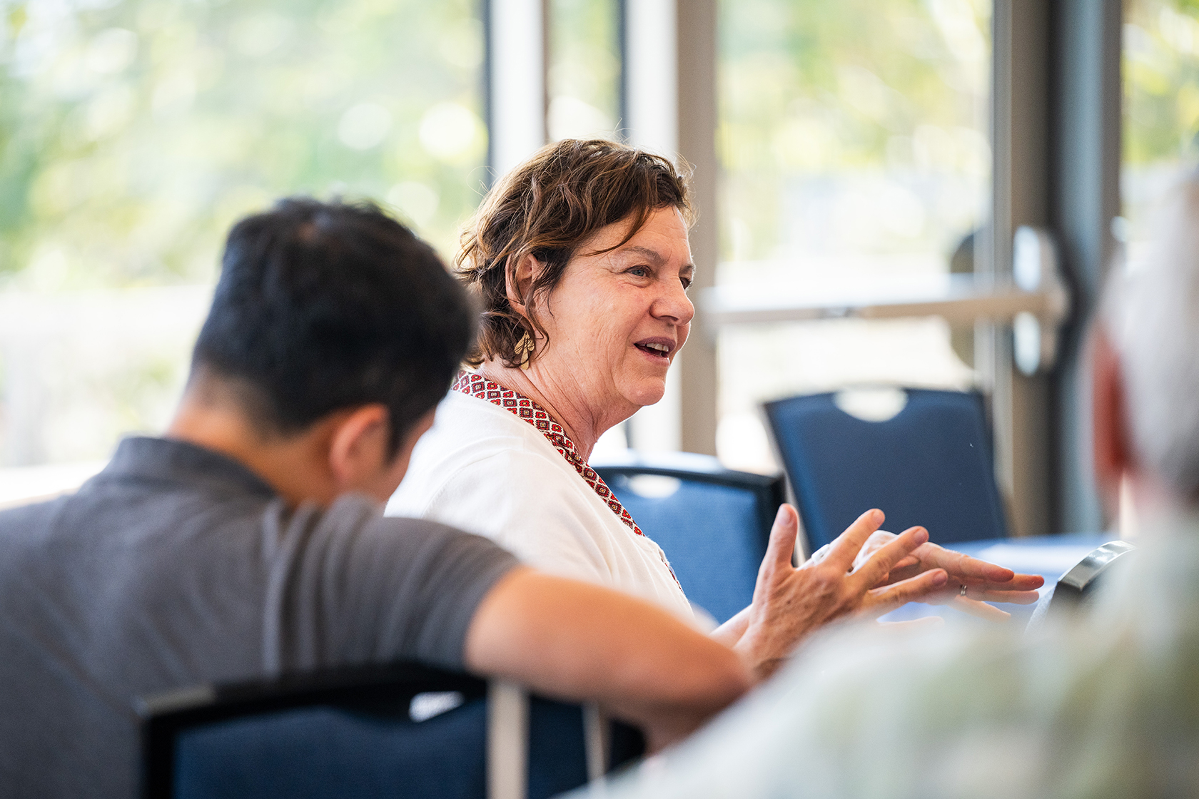 Seated woman in white speaks and gestures with an open hand during discussion