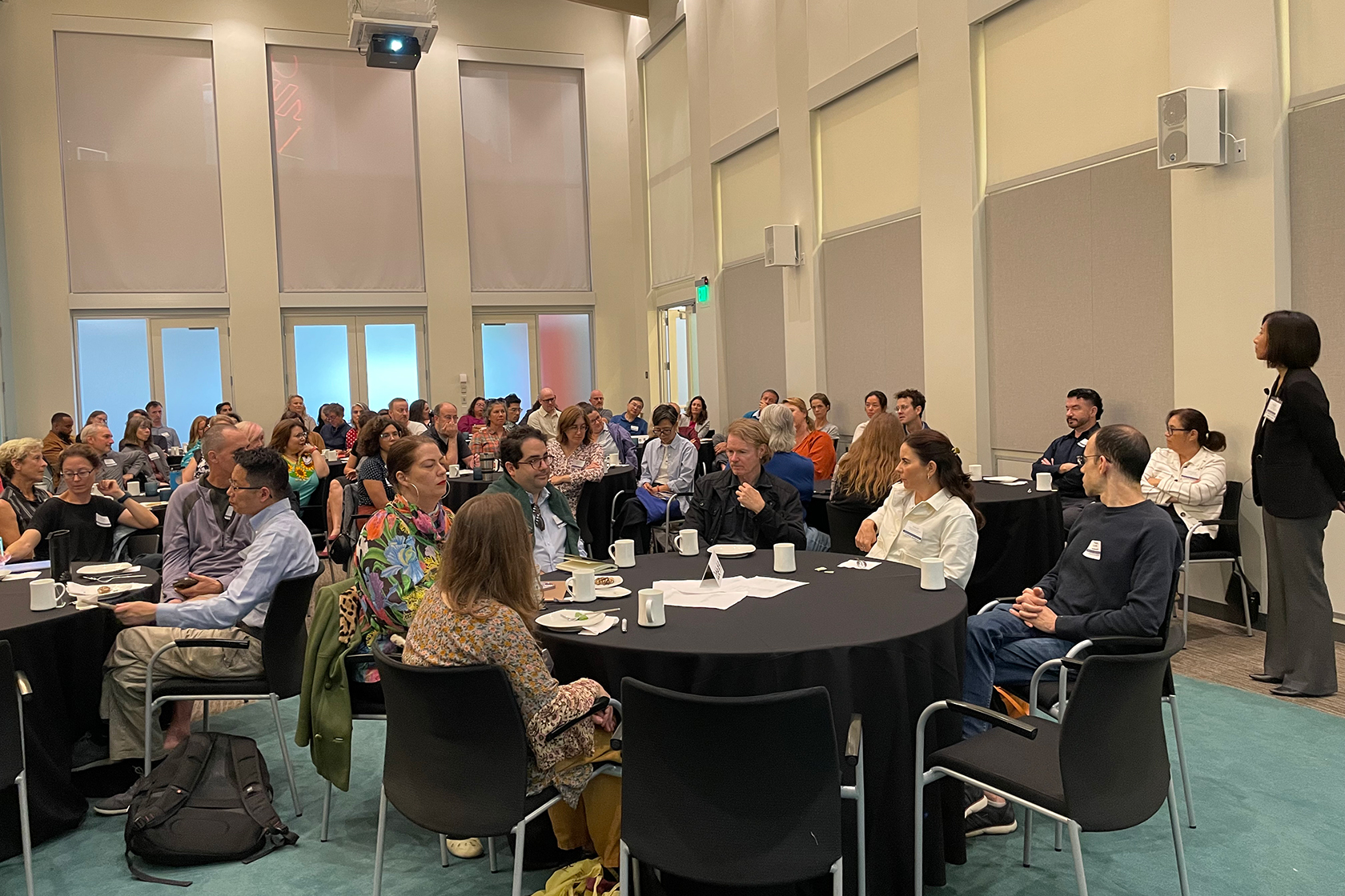 large room of mostly seated people around circular tables