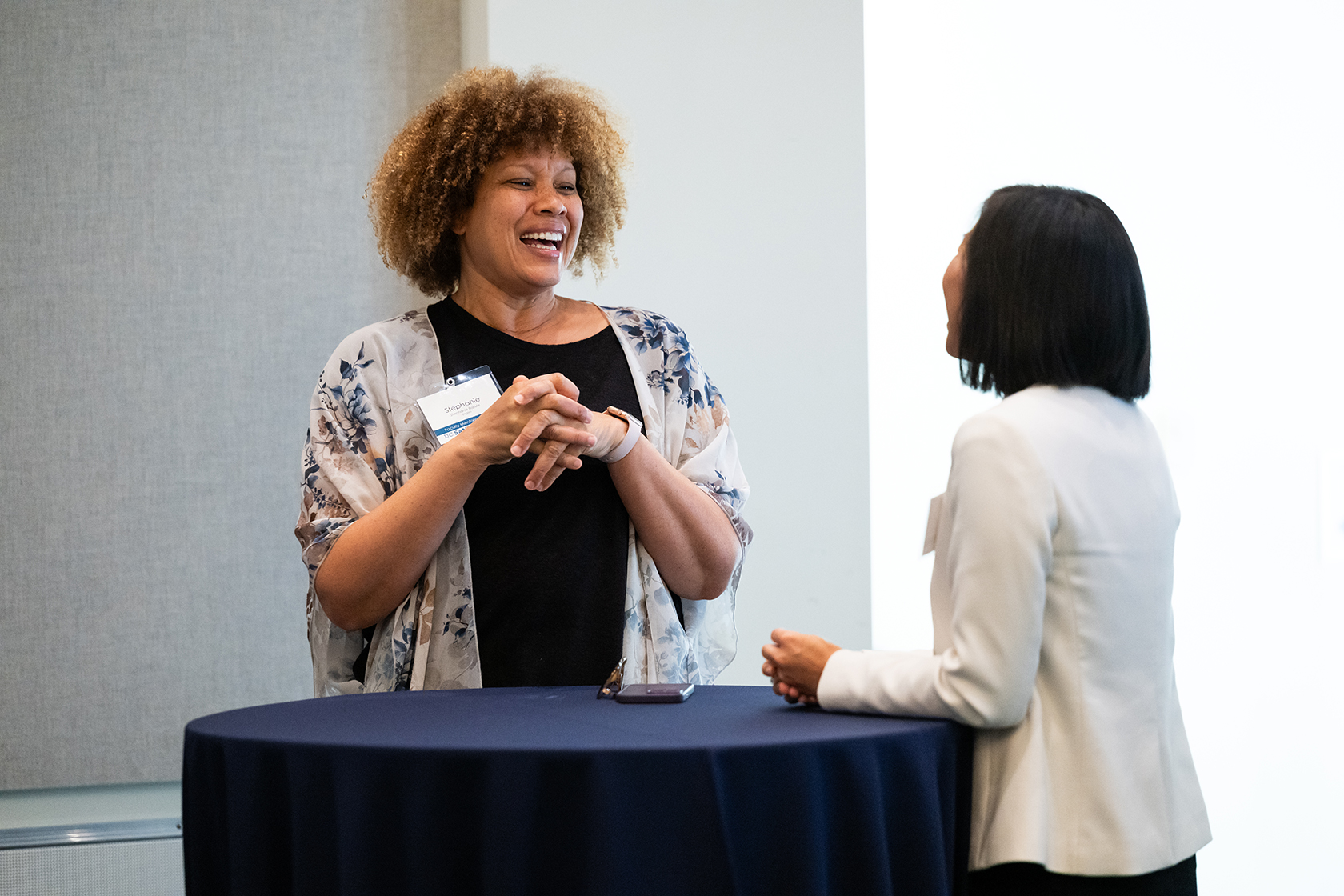 two people standing smiling and talking around a blue circular table