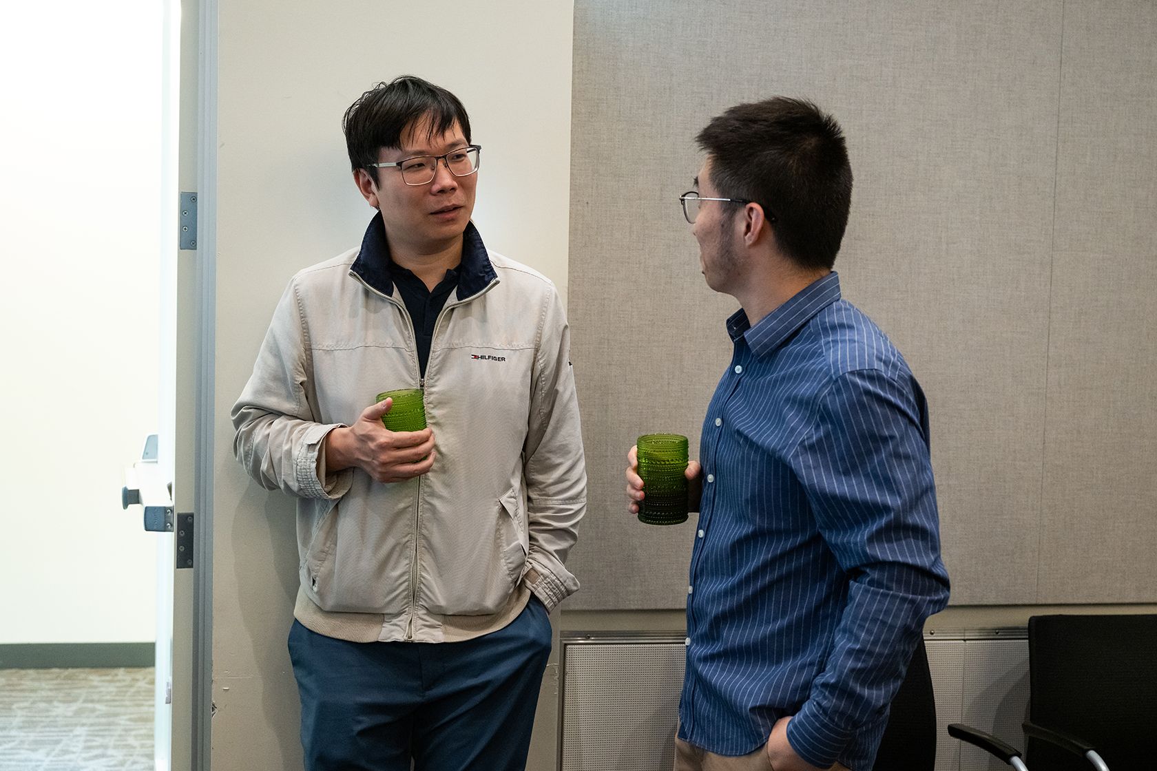 two standing people holding green glasses and chatting