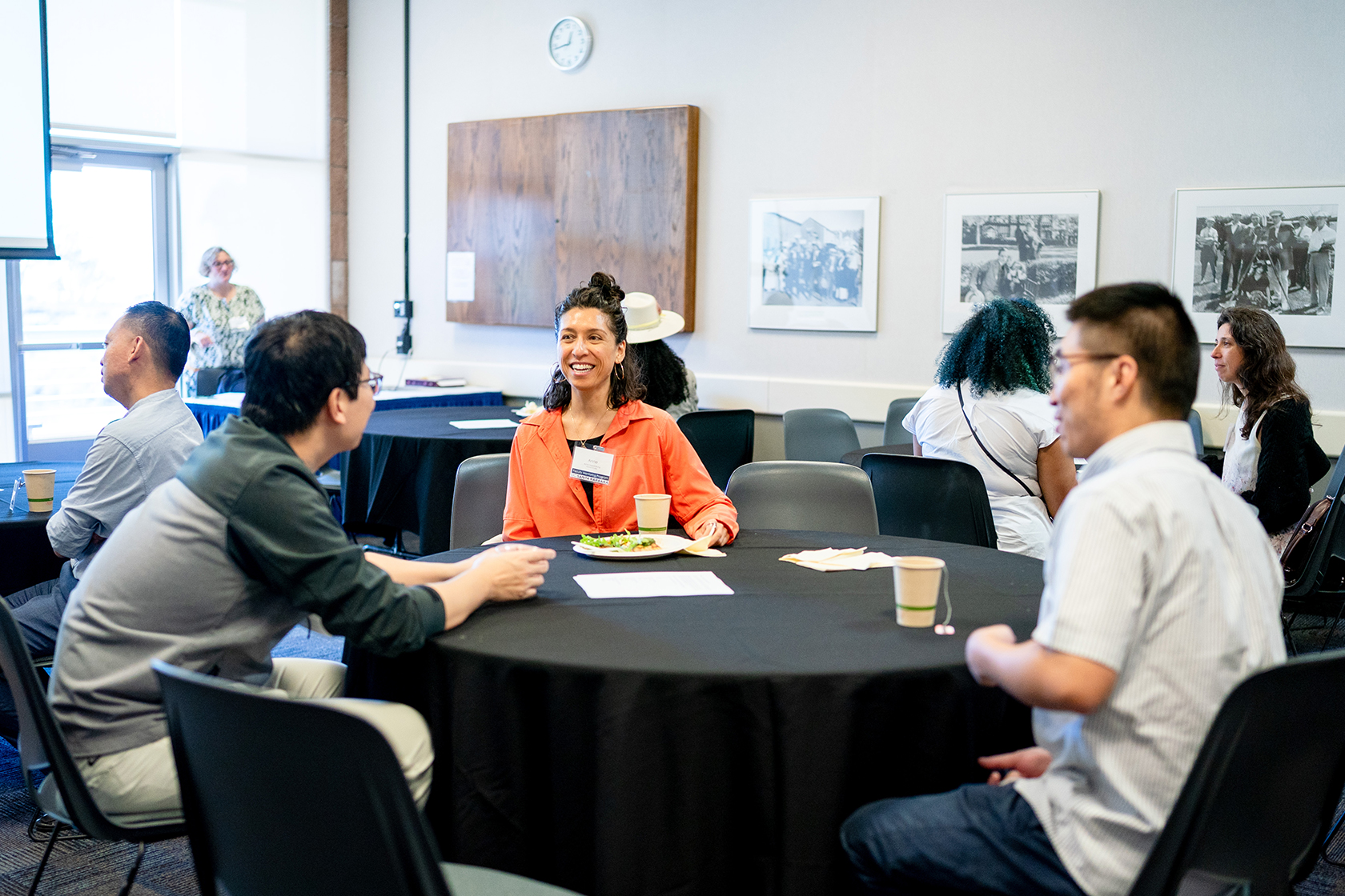 seven people seated around circular tables in smaller groups conversing