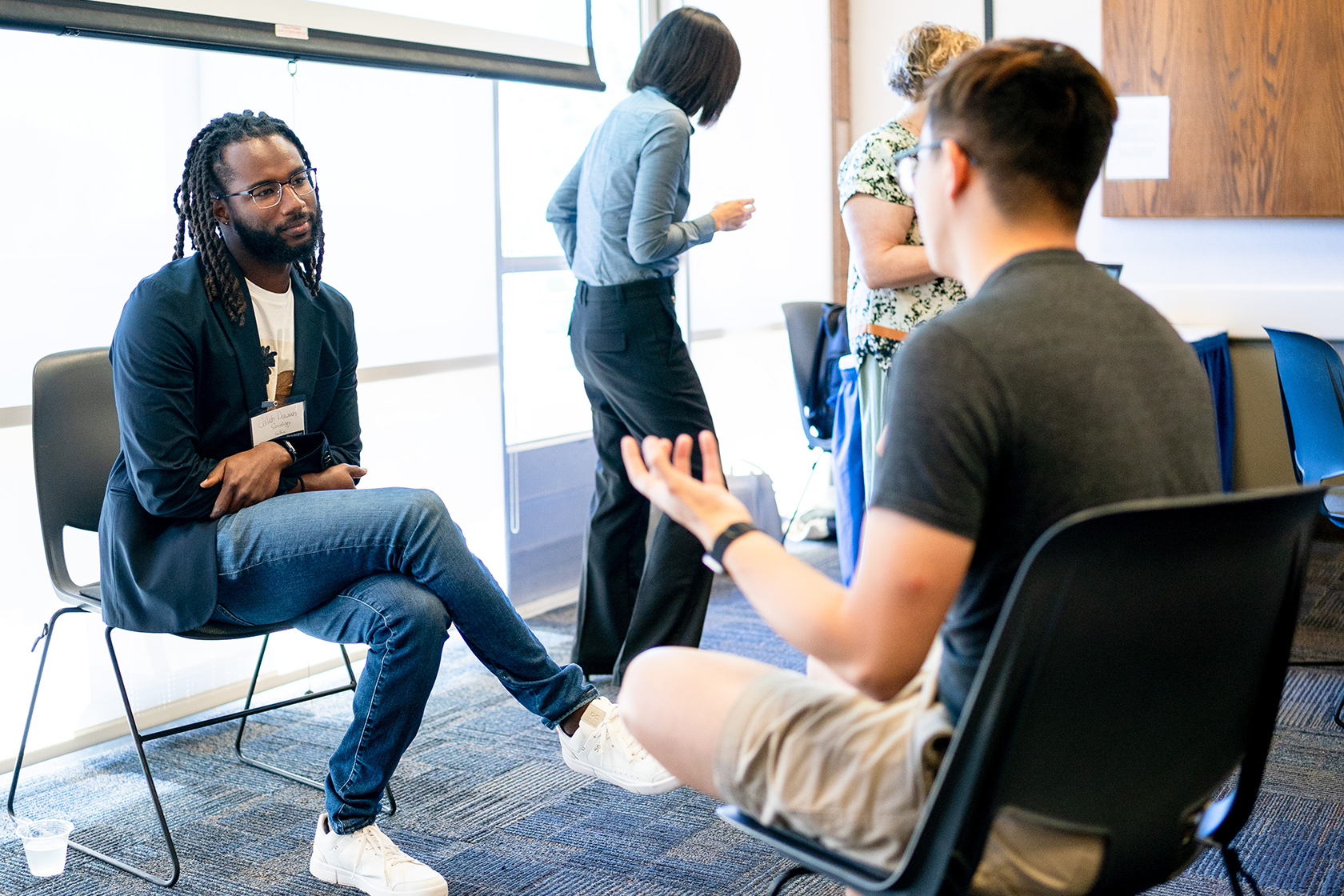 four people pictured two seated conversing with one another