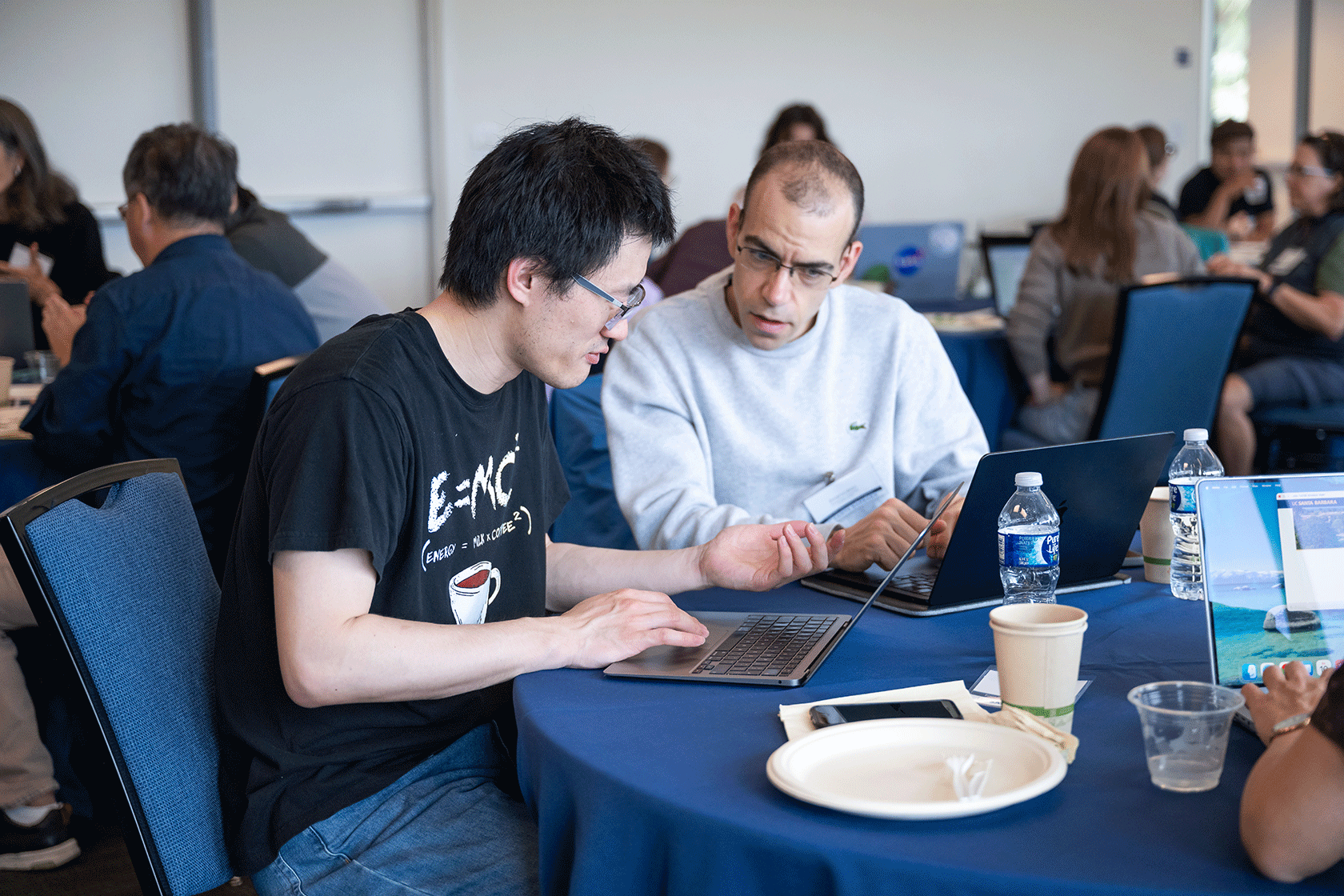 two people seated in front of laptops while talking