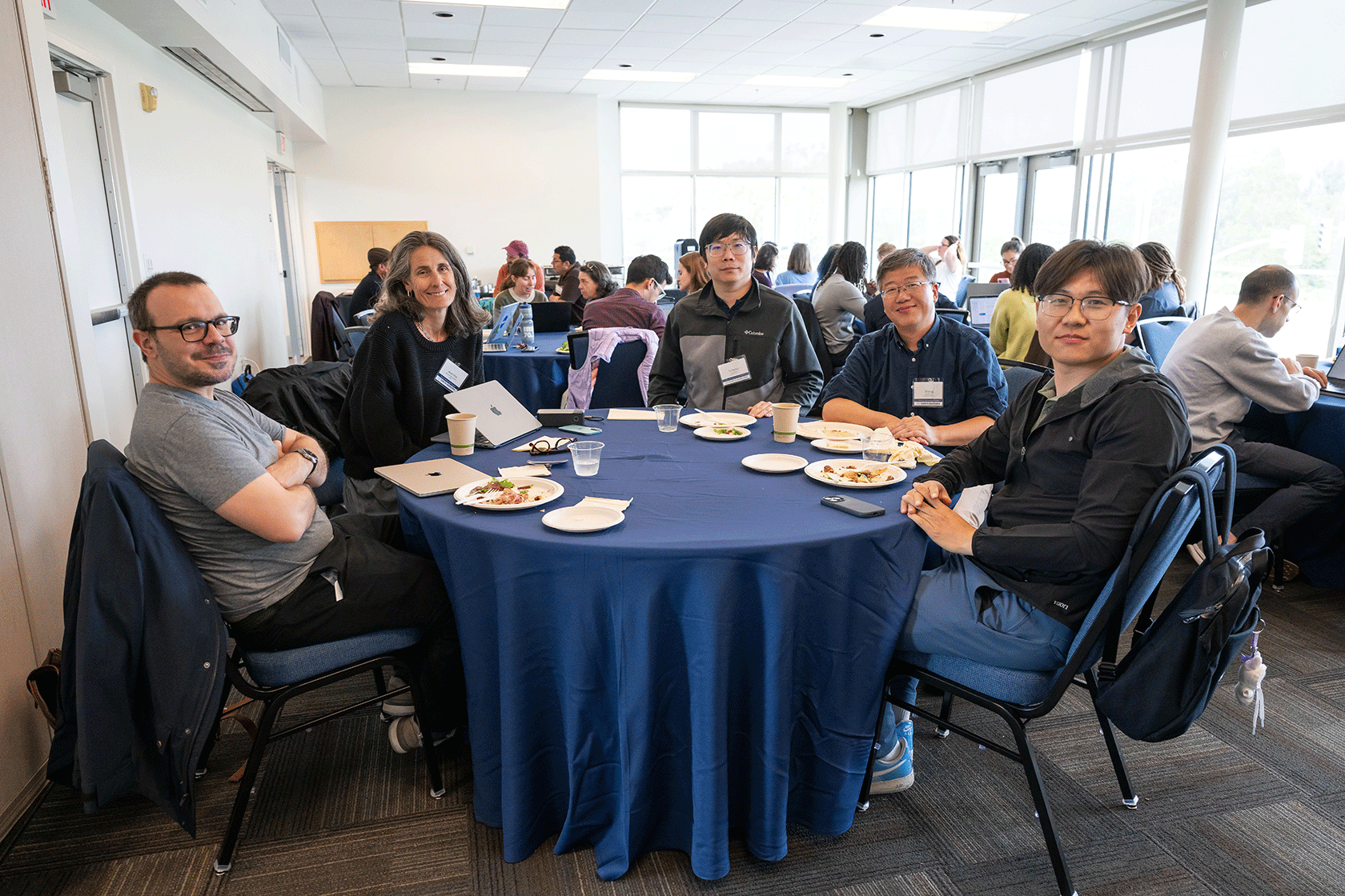 five people seated around a blue circular table smiling for the photo