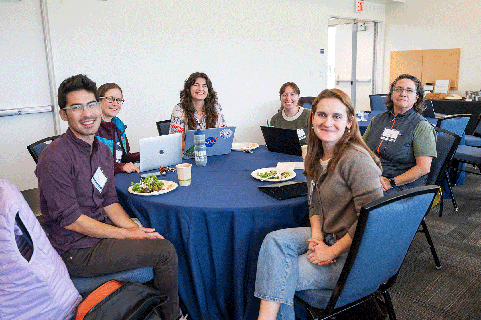 six people seated around a blue circular table smiling for the photo