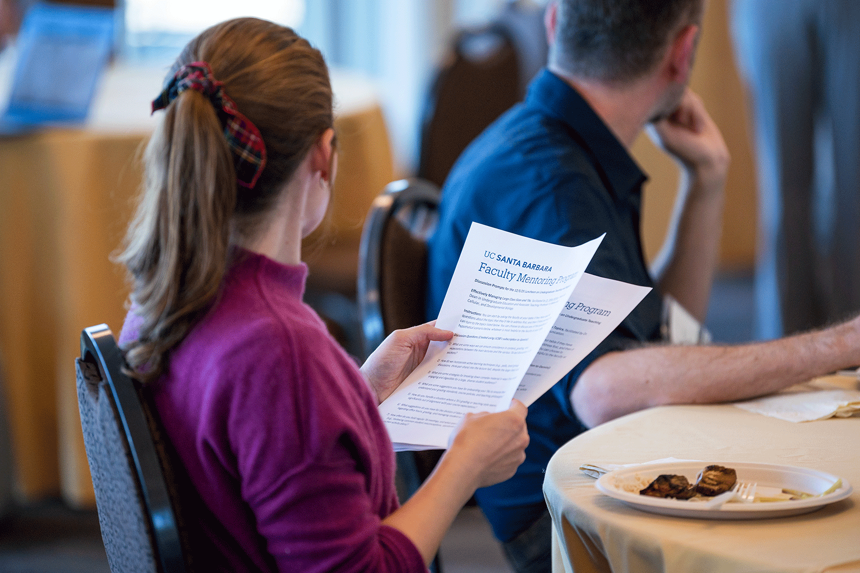 two people seated one holding a stack of papers